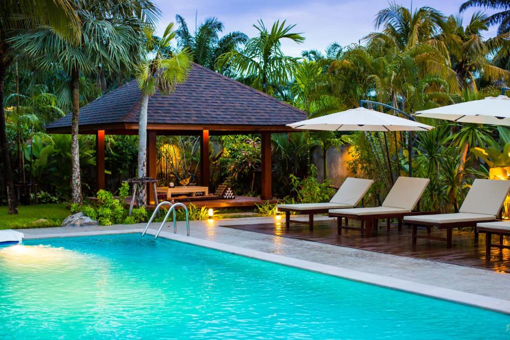 a pool with chairs and umbrellas next to a resort at Villa Pimmada in Ao Nang Beach