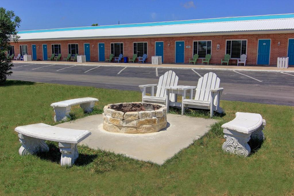 three white chairs and a fire pit in a parking lot at Shark Reef Resort Motel & Cottages in Port Aransas