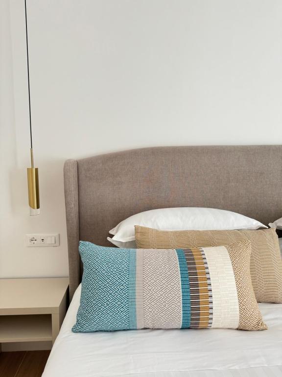 a bed with a gray headboard and pillows on it at Feel Boutique Rooms in Oristano