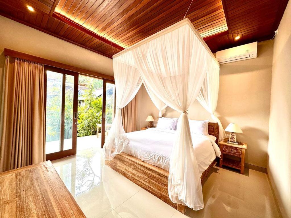 a bedroom with a canopy bed with white curtains at The Madawa Suites in Ubud