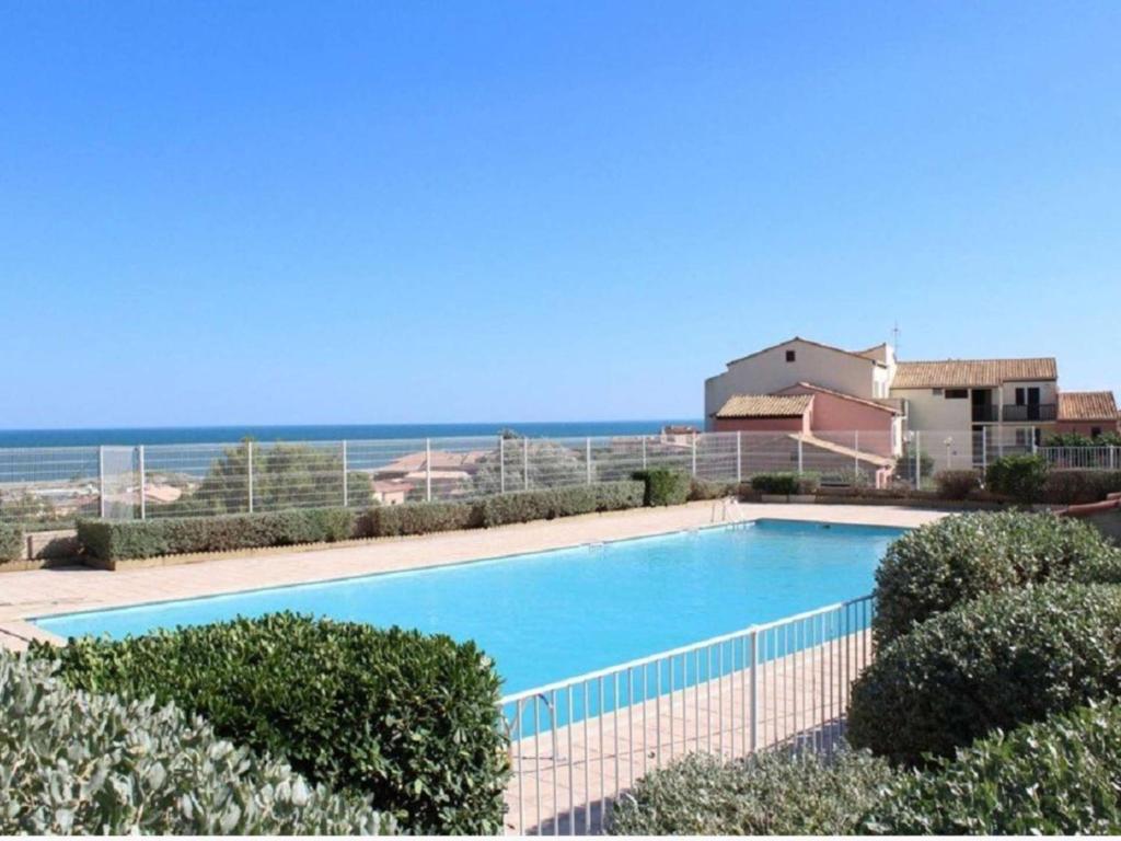 une piscine avec l'océan en arrière-plan dans l'établissement Appartement T2 avec Piscine et Tennis, Proche Plage, Parking Privé - 6 Couchages, Saint Pierre La Mer - FR-1-229D-134, à Fleury