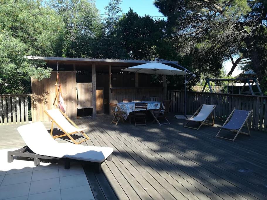 une terrasse avec des chaises, une table et un parasol dans l'établissement Belle villa au Cap Ferret Quartier MIMBEAU, à Lège-Cap-Ferret