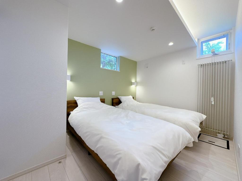 two beds in a bedroom with white walls and a window at GENYA Furano in Nakafurano