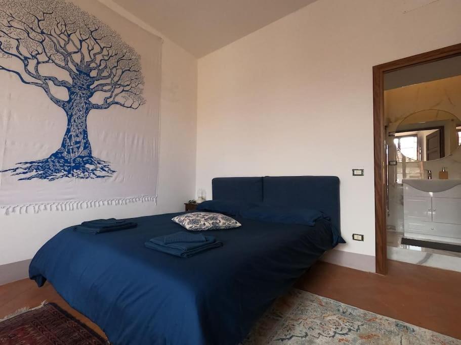 a bedroom with a blue bed with a tree painting on the wall at Suite storica e panoramica - Centro in Pisa