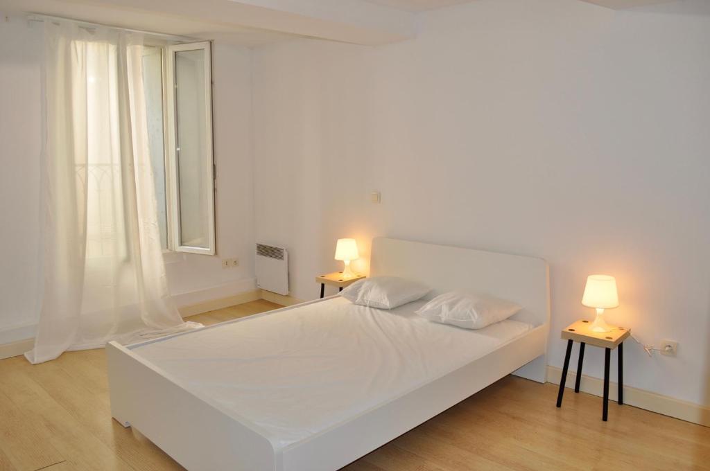a white bedroom with a white bed and two lamps at Le poète roucher in Montpellier