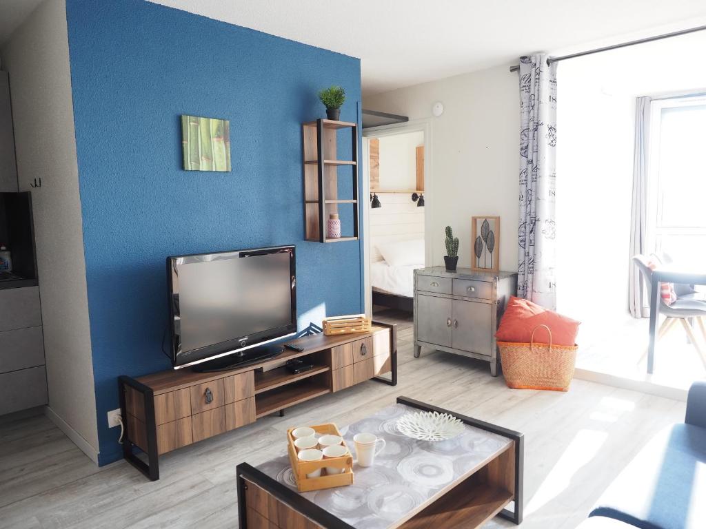Il comprend un salon doté d'une télévision et d'un mur bleu. dans l'établissement A l'Orée des Pins, Appartement Plage du Tanchet, à La Pironnière