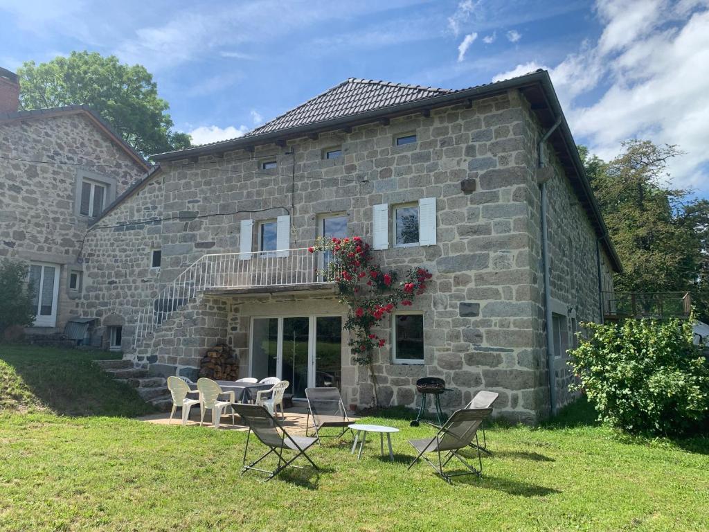 a stone house with chairs and tables in front of it at Ferme au calme à 15mn du Chambon sur Lignon in Saint-Jeures