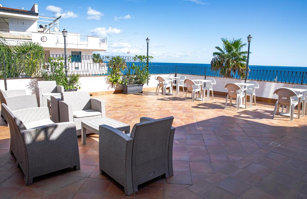 patio z białymi krzesłami i stołami oraz oceanem w obiekcie Palazzo Durante w mieście Letojanni
