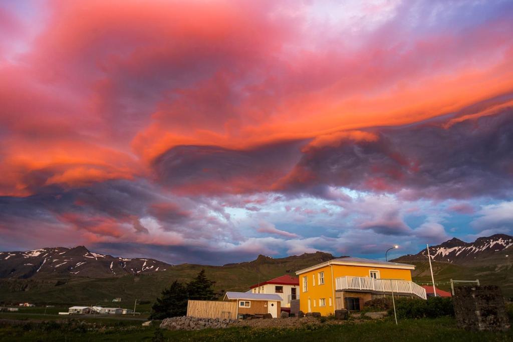 a cloudy sky with a yellow house and mountains at Bjarg Apartments in Grundarfjordur