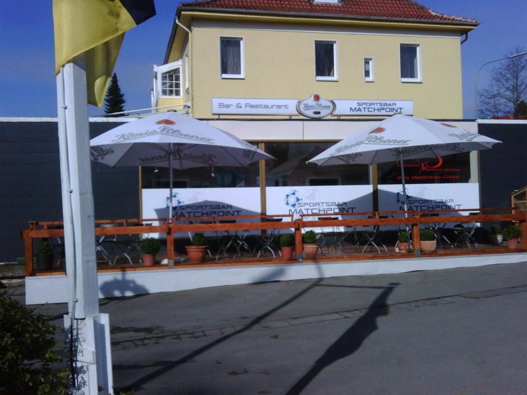 two tables with umbrellas in front of a building at Hotel zur Sportsbar in Horn-Bad Meinberg