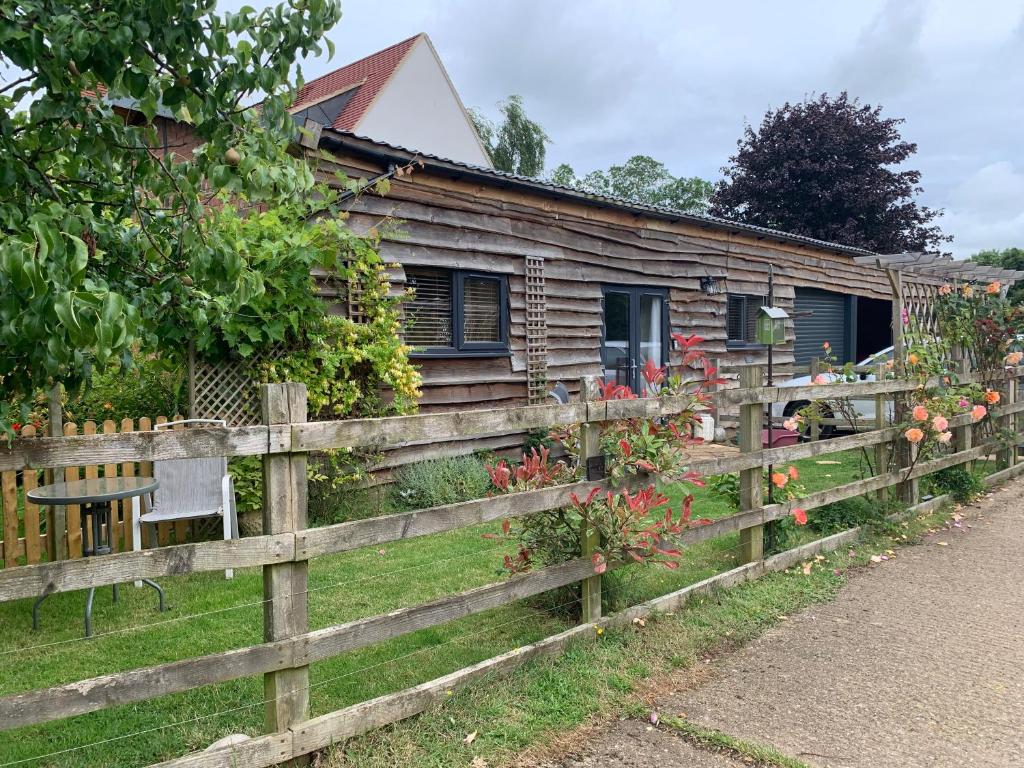 eine Holzhütte hinter einem Zaun mit Blumen in der Unterkunft The Barn at White Rose Cottage in Towcester