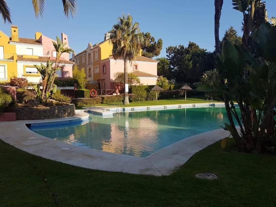 a swimming pool in a yard with palm trees and buildings at Bonita casa adosada in Islantilla