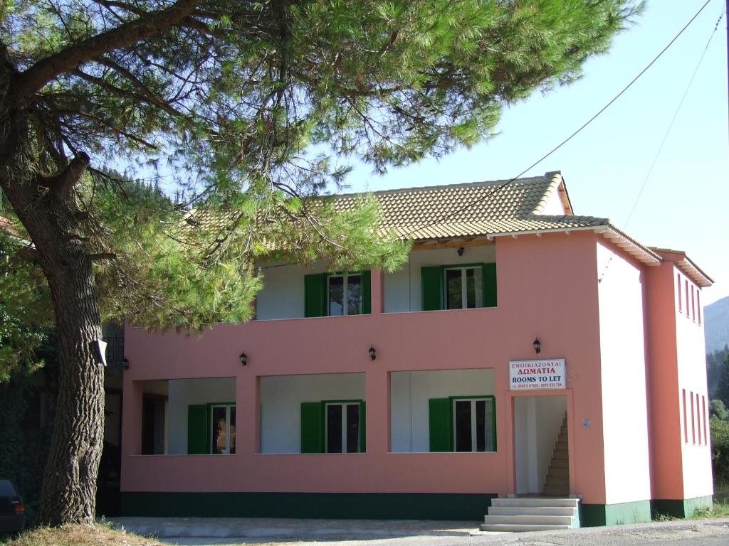 różowy budynek z drzewem przed nim w obiekcie Chalikias Rooms w mieście Asprogerakata