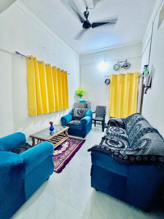 a living room with blue couches and yellow curtains at Its Home - Stay in Aurangabad