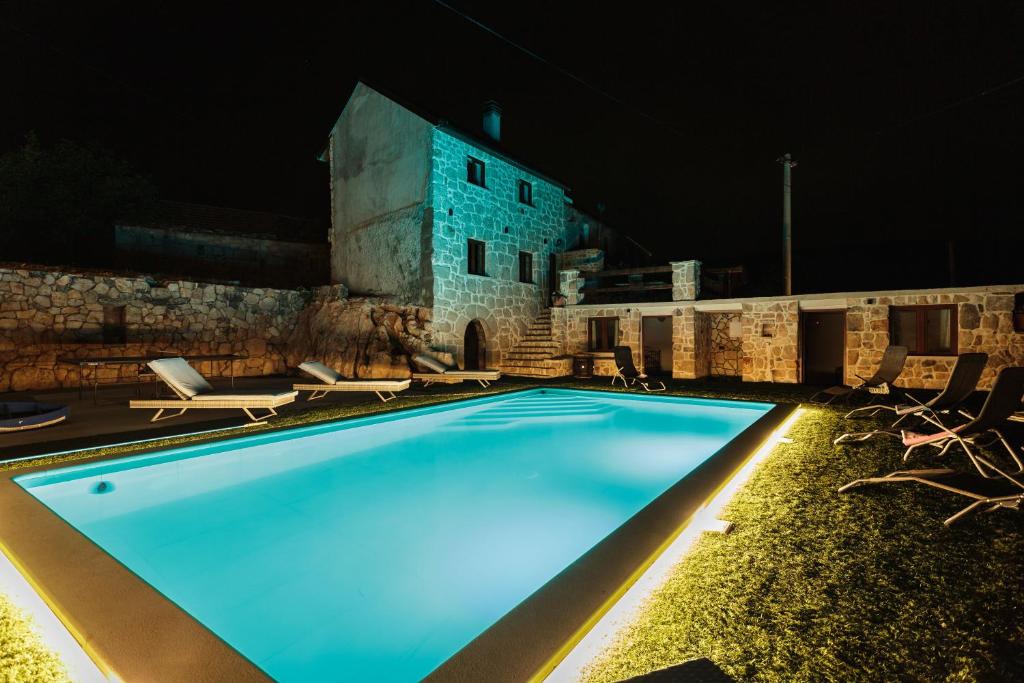 a swimming pool at night with chairs and a building at Villa Stone Valcer in Slivno