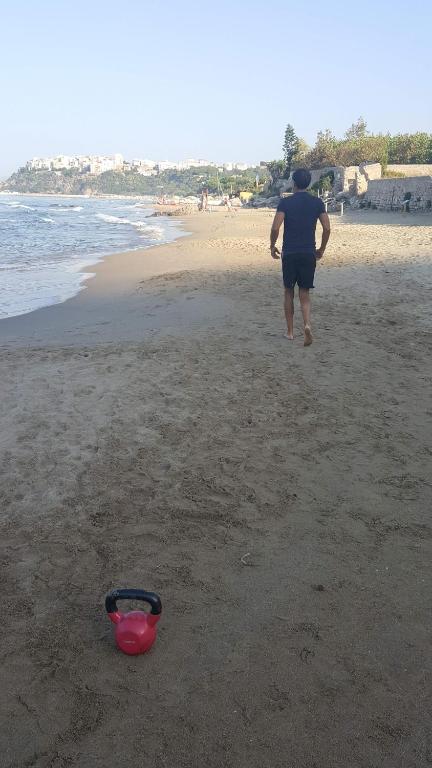 a man walking on the beach with a red bowl at La Flacca Rooms in Sperlonga
