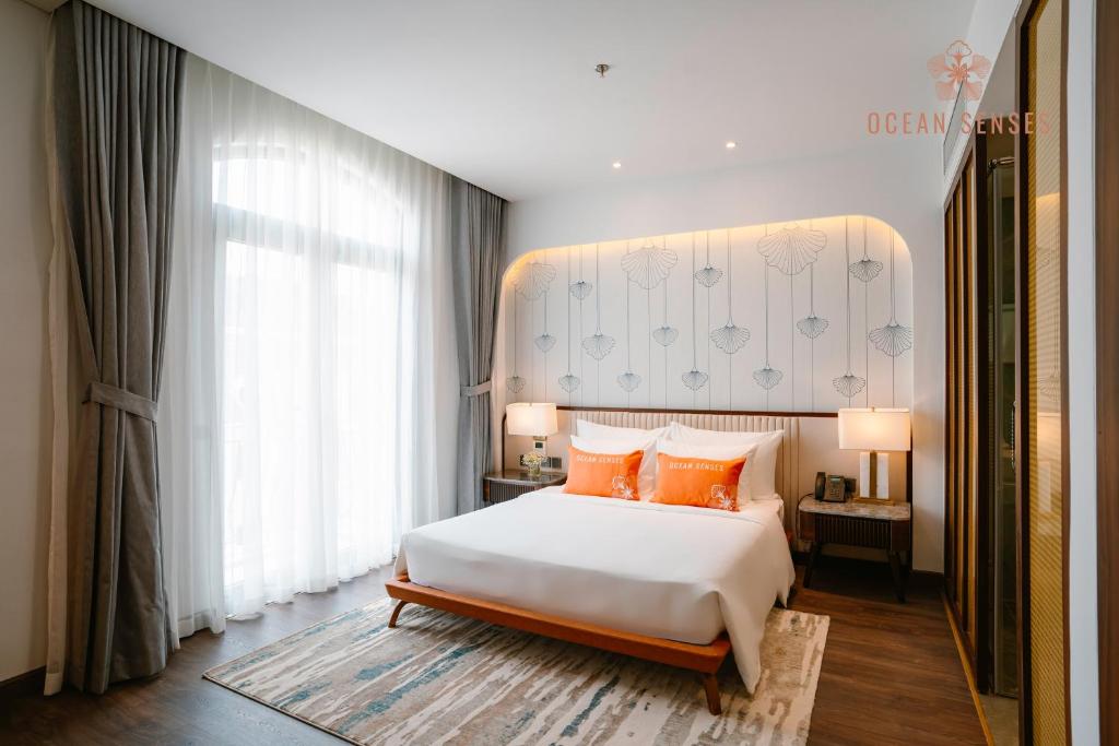 a bedroom with a large white bed with orange pillows at Ocean Senses Hotel in Ðông Thôn