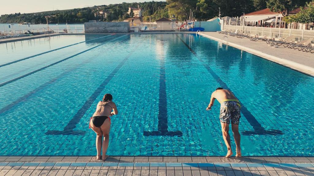 two people are standing in a swimming pool at Olive Family Suites - Hotel & Resort Adria Ankaran in Ankaran