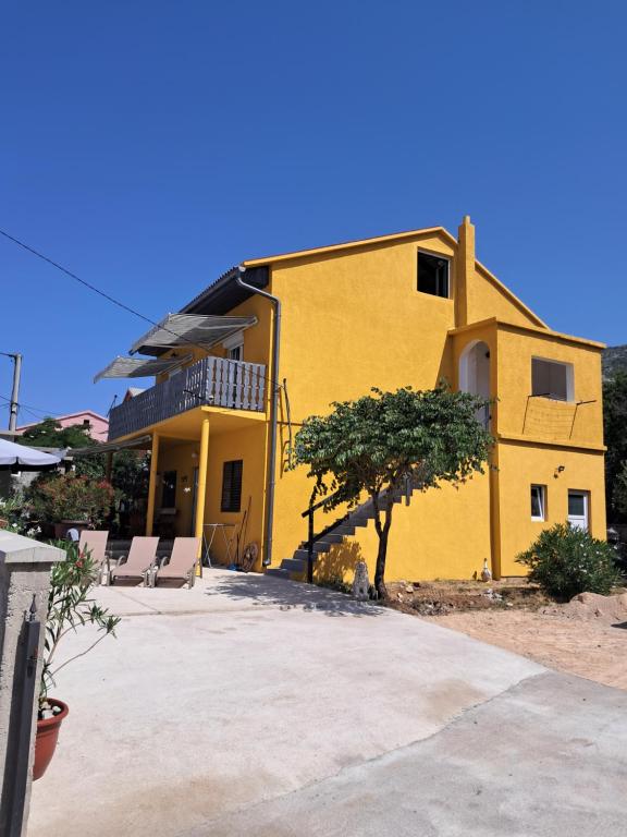 a yellow house with a tree in front of it at Apartments Mara Bela in Karlobag