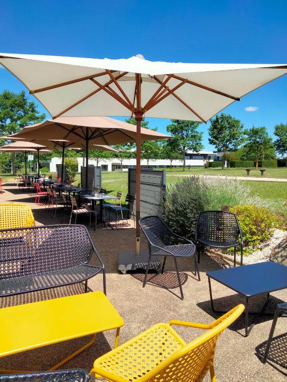 un patio avec tables, chaises et un parasol dans l'établissement Campanile Poitiers - Site du Futuroscope, à Chasseneuil-du-Poitou