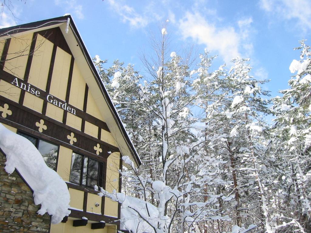 ein schneebedecktes Gebäude neben einigen Bäumen in der Unterkunft Anise Garden in Hakuba