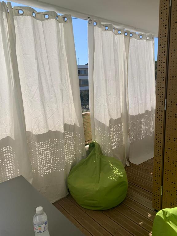 un sac vert posé sur un balcon avec des rideaux blancs dans l'établissement Appartement neuf au calme de Capbreton, à Capbreton