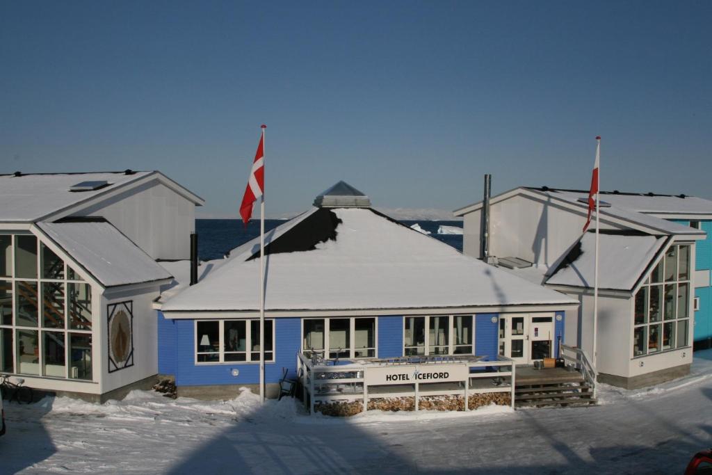 a blue and white building with a flag in the snow at Hotel Icefiord in Ilulissat