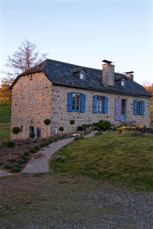 une grande maison en pierre avec des fenêtres bleues et une allée. dans l'établissement Charmant Moulin De Selves, à Auriac