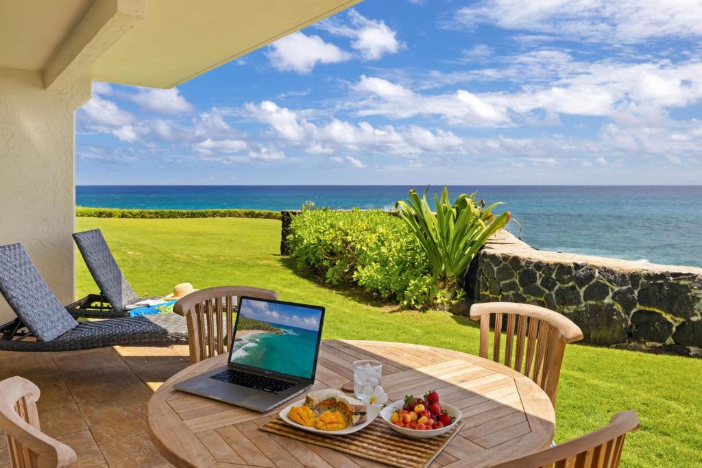 ein Laptop-Computer auf einem Tisch auf einer Terrasse mit Blick auf das Meer in der Unterkunft Poipu Shores 107A in Koloa