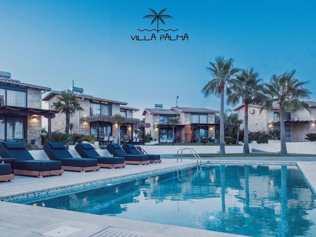 a pool at a resort with lounge chairs and palm trees at Villa Palma in Kallithea Halkidikis
