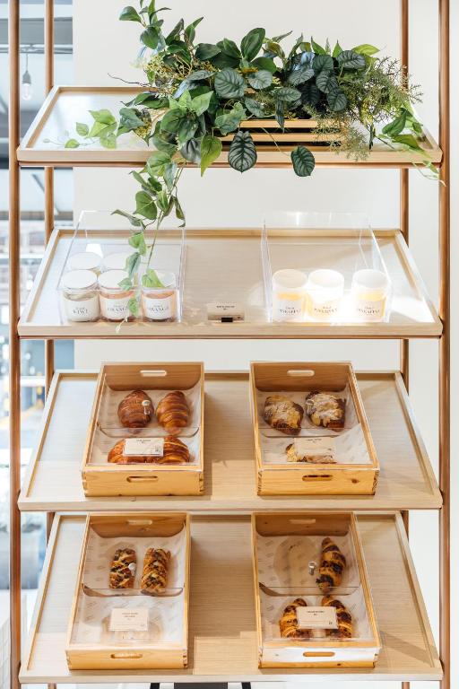 A wooden pastry display with labelled trays and chilled cups beneath trailing plants.