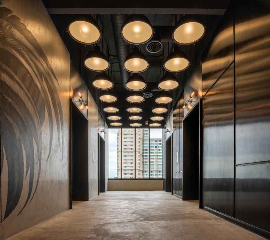 A dark hotel corridor with graphic wall art, circular ceiling lights, and a city-facing window.