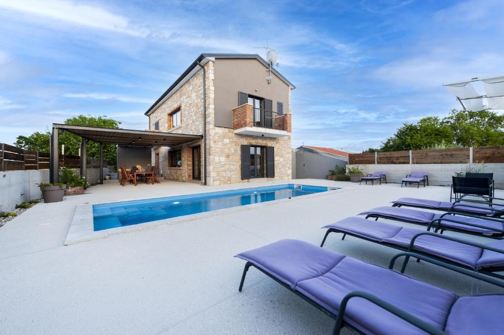 Una piscina con tumbonas moradas al lado de una casa. en Beautiful Villa Baraka with pool near Pazin, en Kanfanar