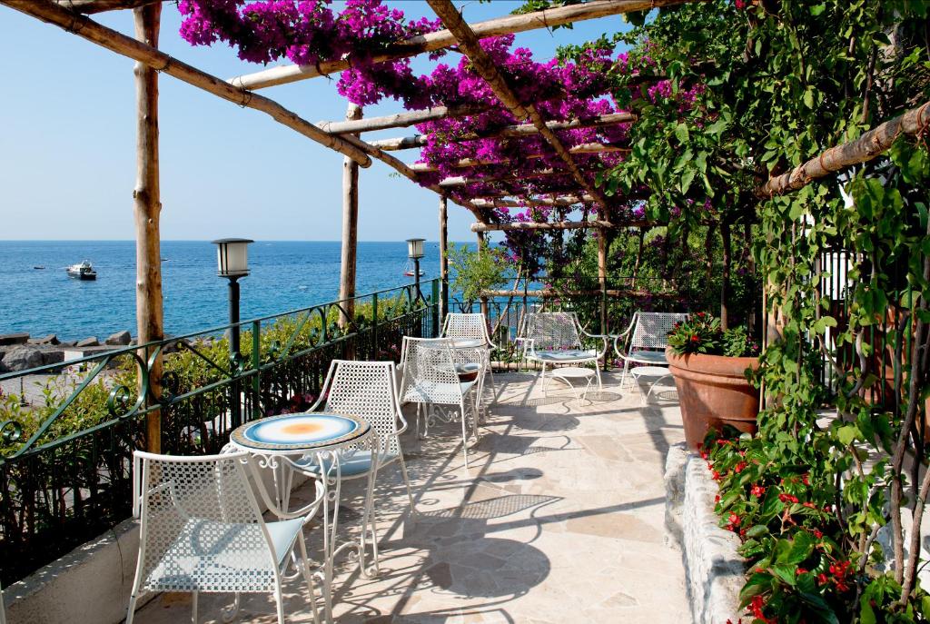 a patio with chairs and tables and purple flowers at Hotel Aurora in Amalfi