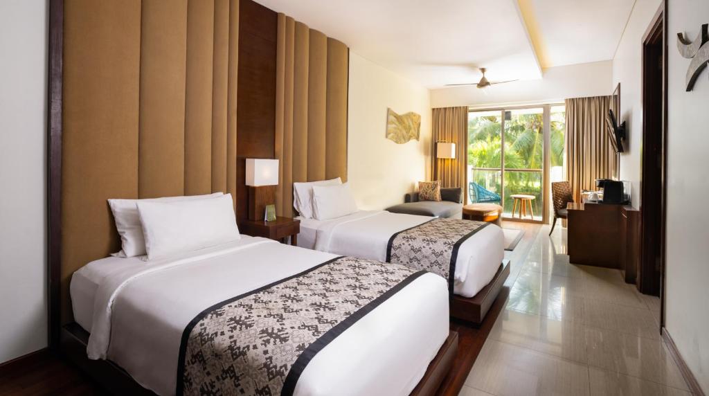 a hotel room with two beds and a balcony at MERUSAKA Nusa Dua in Nusa Dua
