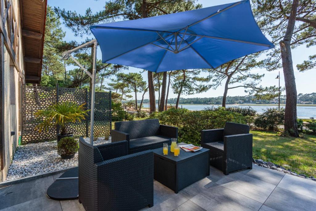 une terrasse avec un parasol bleu, des chaises et une table dans l'établissement La Maison du Lac - Welkeys, à Soorts-Hossegor