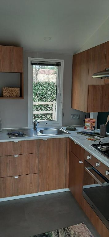 a kitchen with wooden cabinets and a sink and a window at Mobil home neuf 6 personnes in La Tremblade