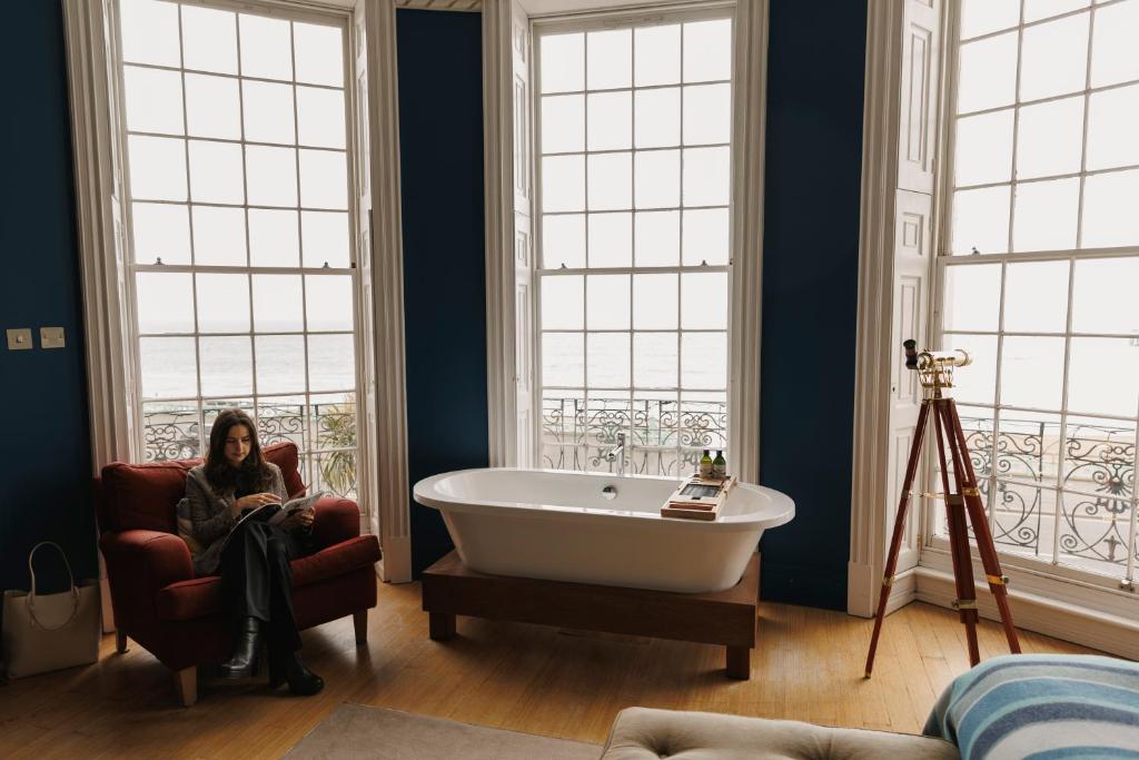 a woman sitting in a chair next to a tub in a bathroom at Drakes Hotel in Brighton & Hove
