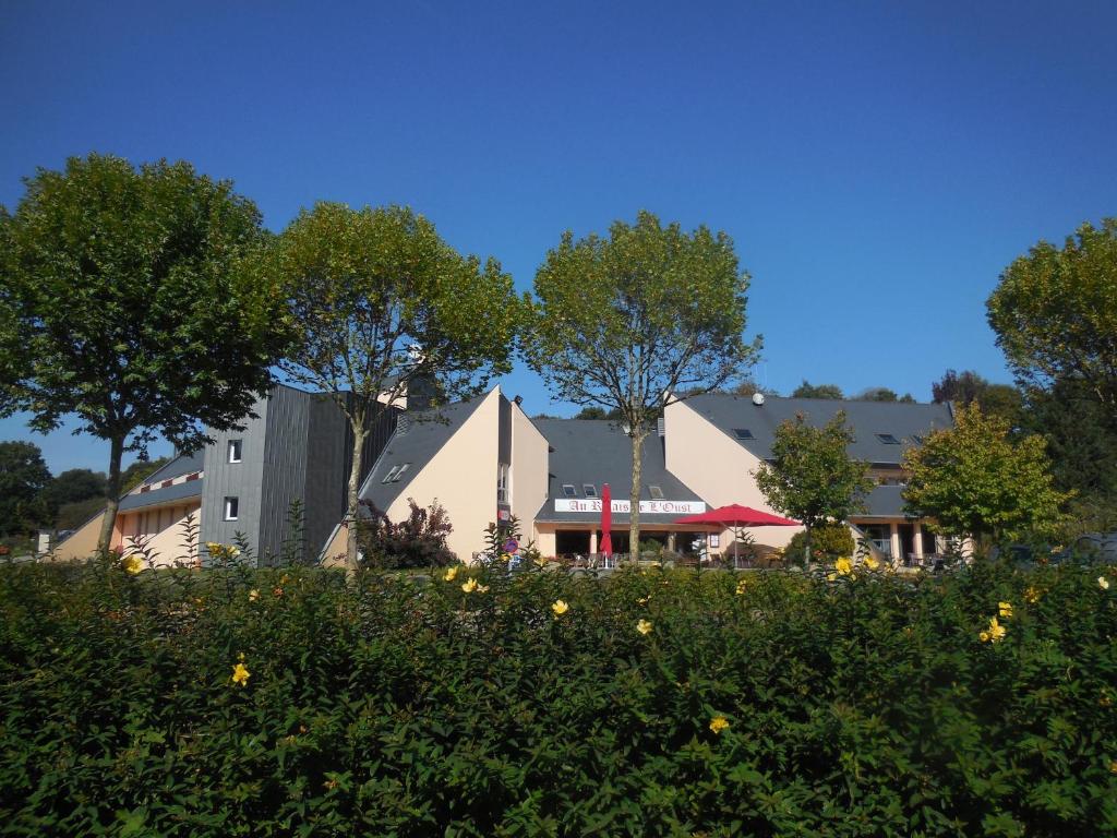 Au Relais de l'Oust في Lanouée: مبنى يوجد به اشجار خلف حقل من الزهور