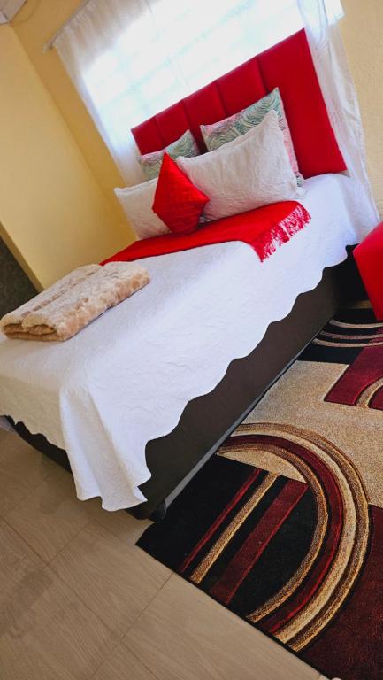 a bed with red and white pillows and a window at Goodlife guest house in klerksdorp in Klerksdorp