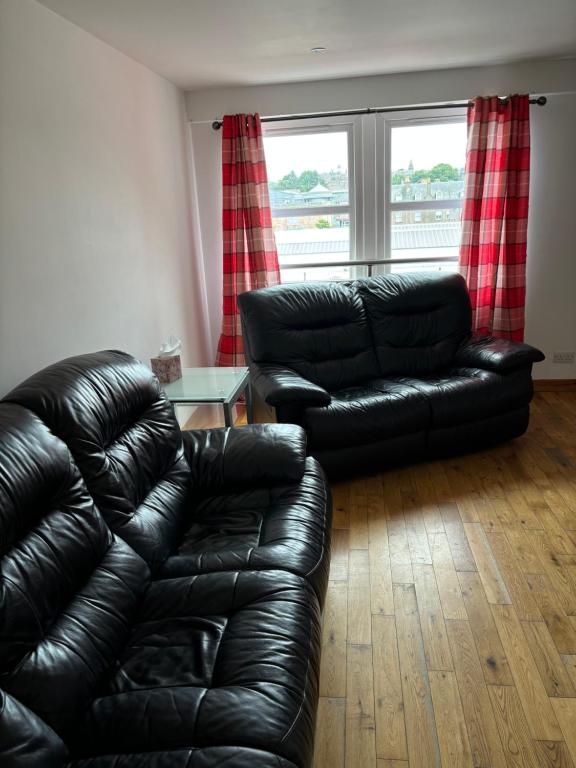 a living room with a black leather couch and a table at MacIver City Apartments Farraline Court in Inverness