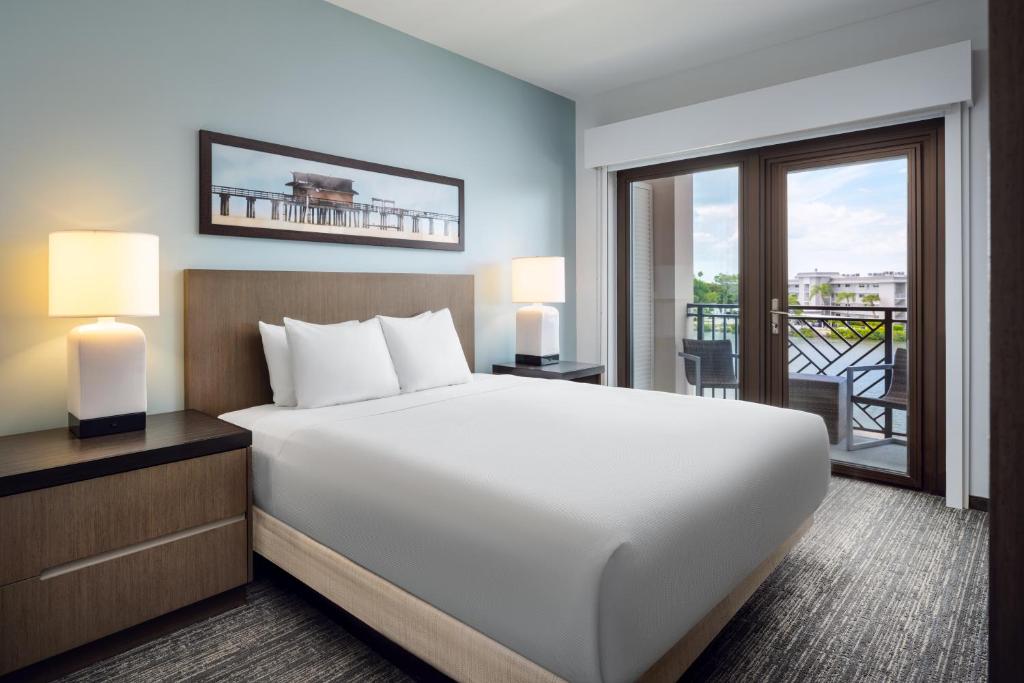 a bedroom with a large white bed and a balcony at Hyatt House Naples 5th Avenue in Naples