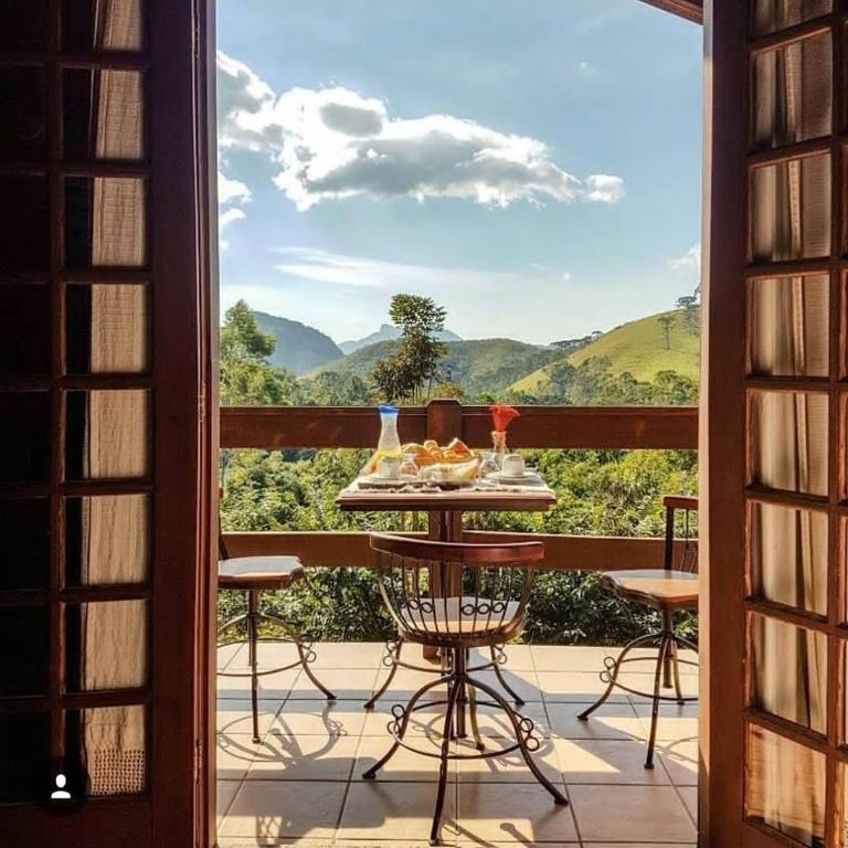 a table on a balcony with a view of the mountains at Chalés Nó da Madeira in Visconde De Maua