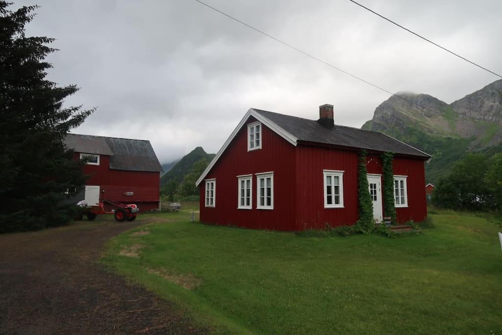 una casa roja en un campo con montañas al fondo en Lillehuset, en Kabelvåg