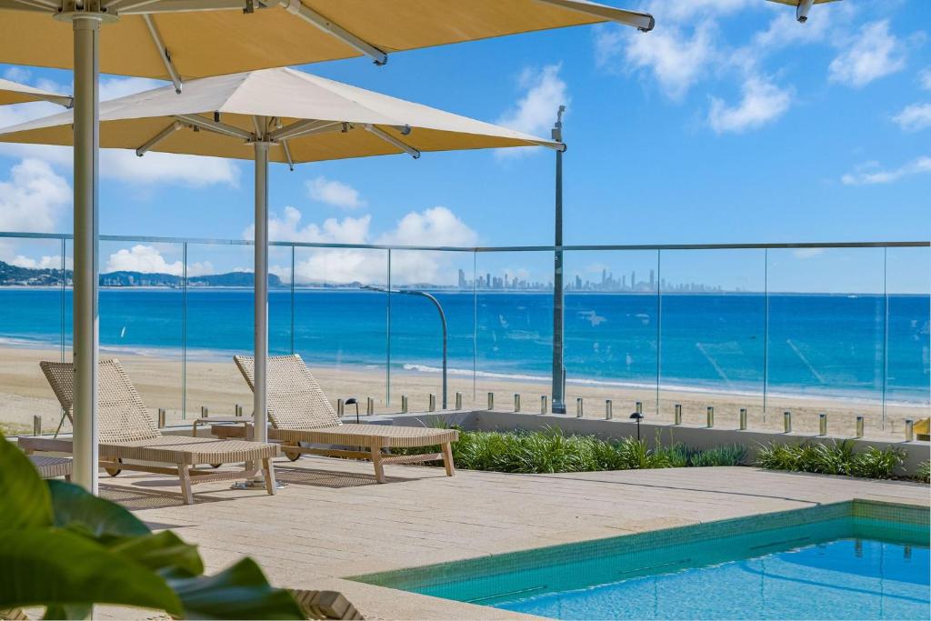 a pool with chairs and umbrellas next to a beach at Miles at Kirra Point 303 in Gold Coast