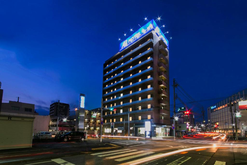 un bâtiment éclairé dans une rue de la ville la nuit dans l'établissement AB Hotel Ichinomiya, à Ichinomiya
