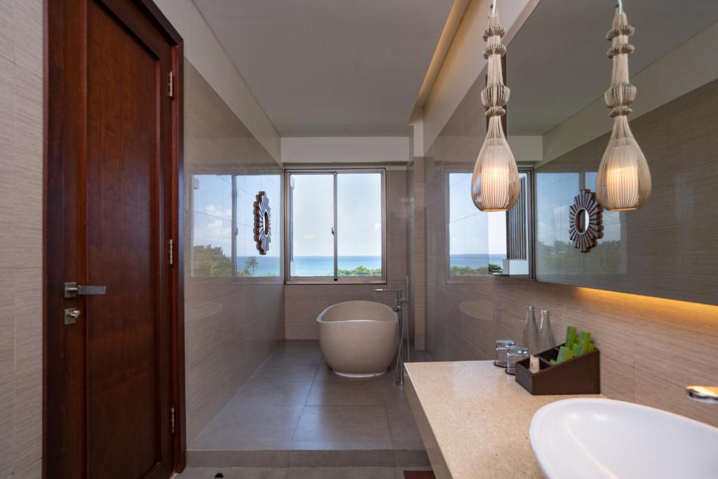 a bathroom with a tub and a sink and windows at MERUSAKA Nusa Dua in Nusa Dua