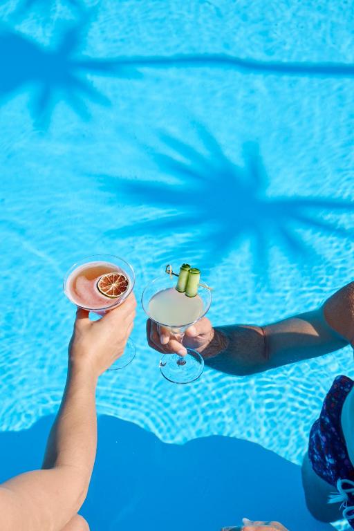 une personne prenant un verre devant une piscine dans l'établissement Princess Resort, Santikos Collection, à Agia Paraskevi
