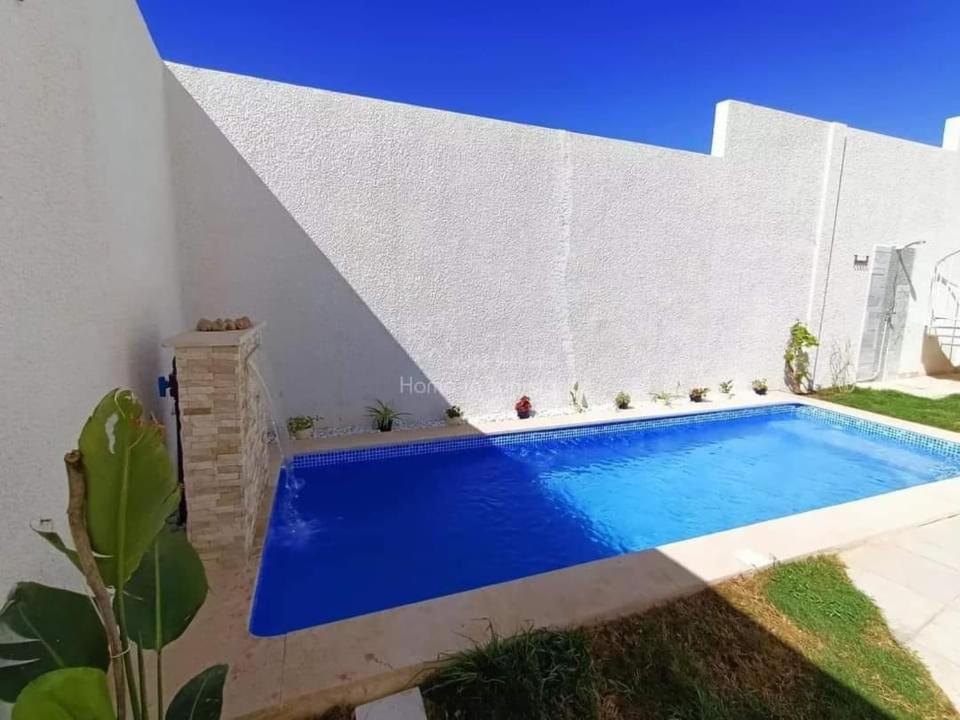 a swimming pool in the backyard of a house with a white wall at Villa Piscine Hergla in Akouda
