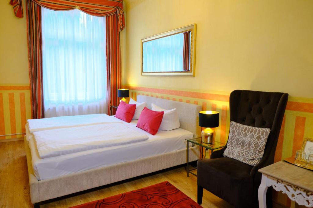 a bedroom with a bed with pink pillows and a chair at Anno 1900 Hotel Babelsberg in Potsdam